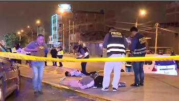Policías en chalecos fluorescentes con la palabra "POLICIA" acordonan una calle oscura con cinta amarilla, con cuatro personas boca abajo en el suelo y varios vehículos