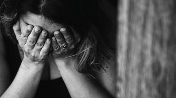 Mujer cubre su rostro con ambas manos. Un anillo se observa en el dedo anular de su mano derecha. La imagen es en blanco y negro con fondo oscuro.