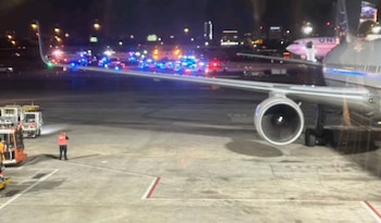 Vista nocturna de un avión en la pista de un aeropuerto, con múltiples vehículos de emergencia con luces parpadeantes y personal en el suelo