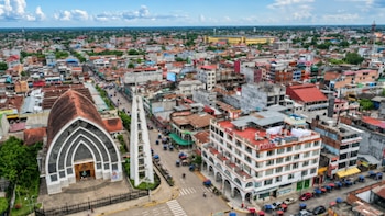 Vista aérea de una catedral con techo abovedado, una torre campanario blanca, calles con mototaxis y edificios urbanos bajo un cielo despejado