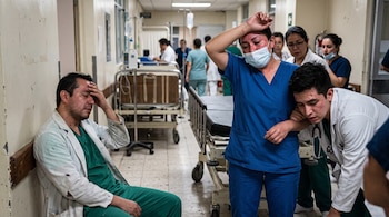 Varios profesionales de la salud con batas y uniformes quirúrgicos en un pasillo de hospital muestran manchas rojas en la piel.