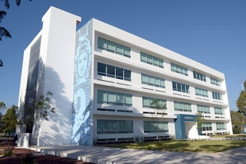 Edificio moderno blanco de múltiples pisos con ventanas, un mural azul abstracto en un lateral y un letrero azul que dice 'MULTIAULAS 4' en la entrada