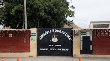 Portón negro con inscripciones del colegio Santa Rosa de Lima, muros de ladrillo rojo, un árbol y conos de tránsito naranjas.