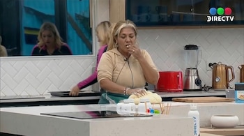 Gladys La Bomba Tucumana, con el cabello rubio y canoso, amasa con las manos mientras se lleva un trozo de masa a la boca en una cocina moderna.