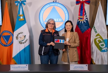 Dos mujeres sostienen una carpeta con las banderas de Taiwán y Guatemala. Banderas de Guatemala y Taiwán, logos de CONRED e ICDF, placas con nombres