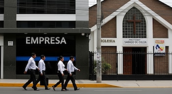 Cuatro personas, dos hombres y dos mujeres, caminan de perfil por una acera frente a un edificio con el letrero "Empresa" y una iglesia con cartel de "Iglesia" y "Sábado de Culto".