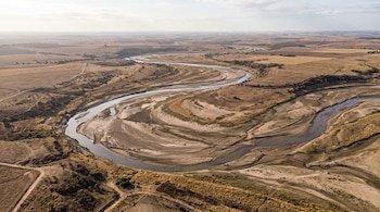 Vista aérea de un río meandroso con cauce estrecho y amplias zonas de arena y sedimento expuesto, rodeado de campos secos.