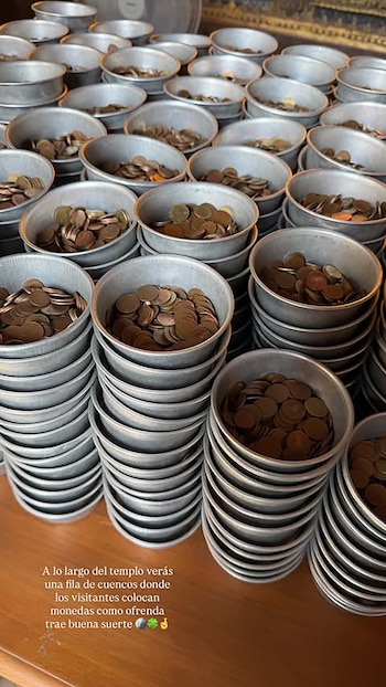 Vista superior de múltiples cuencos metálicos, algunos apilados y otros llenos de monedas de bronce, sobre una superficie de madera en un templo