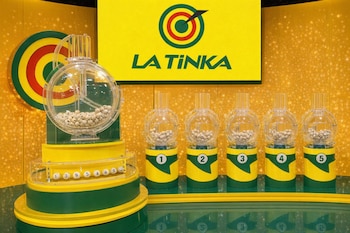Máquinas transparentes de extracción de números con bolas blancas, una base amarilla y verde, y un cartel con el logo de La Tinka en un estudio.