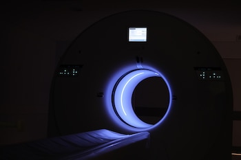 Un tomógrafo circular con luz azul en el túnel central y una camilla extendida en una habitación en penumbra