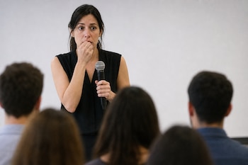 Una mujer vestida de negro sostiene un micrófono frente a la audiencia difuminada que ocupa el primer plano.