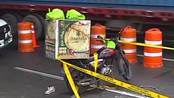 Una motocicleta en el suelo junto a una caja grande, conos de tráfico anaranjados y blancos, cinta policial amarilla y un zapato deportivo blanco