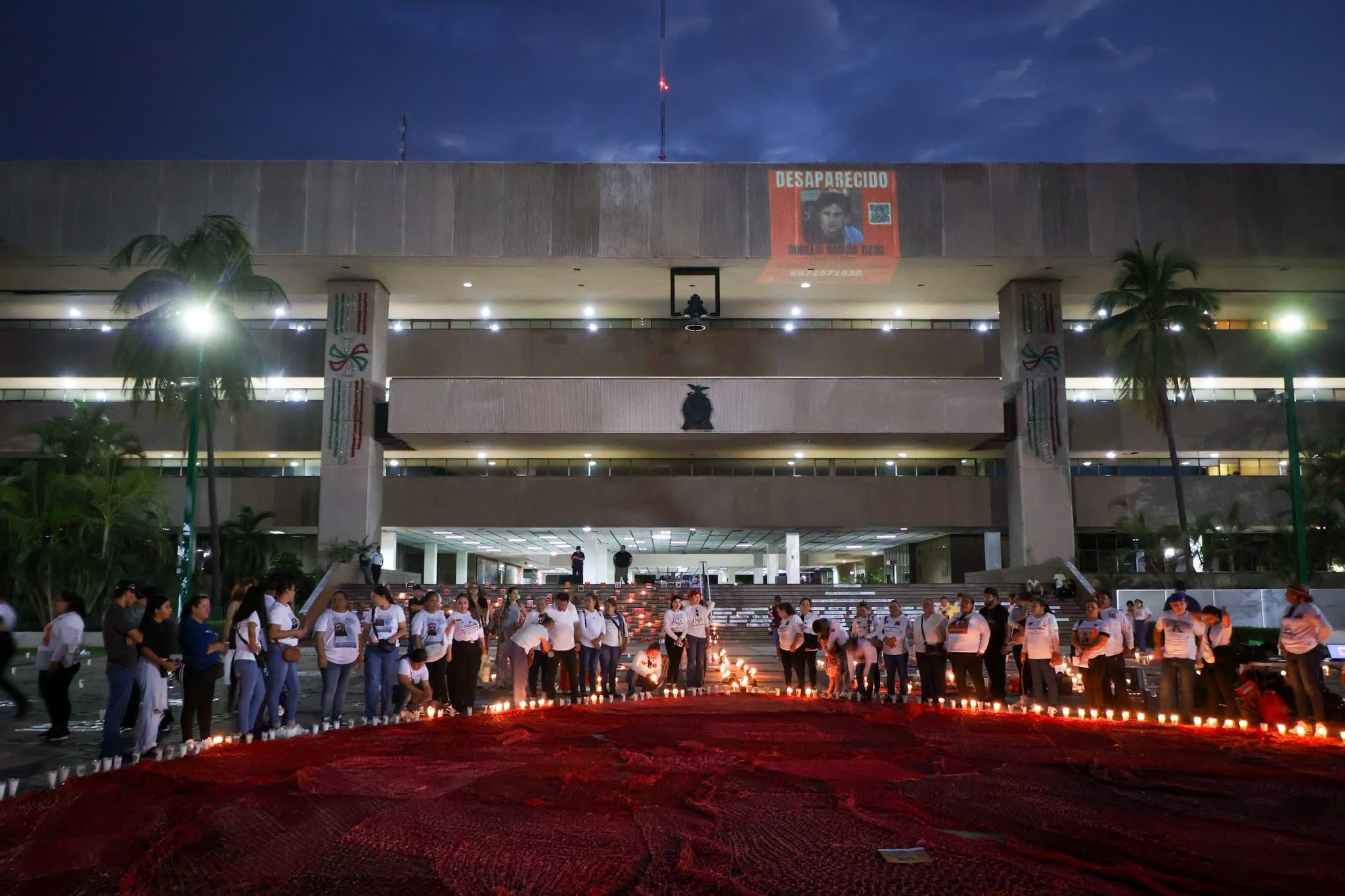 Familias de personas desaparecidas realizaron la noche del sábado 29 de agosto una vigilia con velas y fotografías en la explanada del Palacio de Gobierno de Sinaloa, en Culiacán, para exigir verdad, justicia y avances en las investigaciones, así como la localización e identificación de sus familiares ausentes. La protesta ocurrió horas después del ataque contra la buscadora Alma Rosa Rojo Medina. (Crédito: facebook | La Pared)