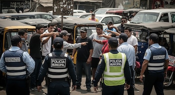 Agentes de policía municipal y serenazgo en un estacionamiento informal con mototaxis y vehículos, rodeados de civiles que señalan a un hombre.
