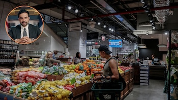 Interior de un supermercado con clientes, exhibición de frutas y verduras, y una cesta de compra verde. Recuadro con retrato de Zohran Mamdani, traje y corbata