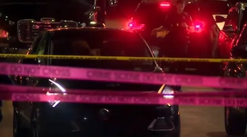 Cintas de protección policial acordonan una calle nocturna entre automóviles y un agente de policía al fondo