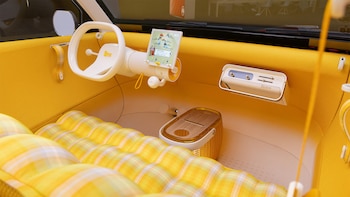 Interior de un automóvil con volante blanco, pantalla digital, salpicadero amarillo, radio de estilo antiguo y asientos tapizados a cuadros