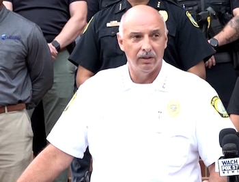 Un oficial de policía en uniforme blanco habla ante micrófonos rodeado por otros agentes durante una conferencia de prensa