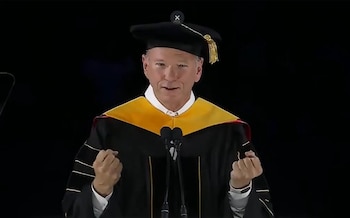 Eric Schmidt, con toga y birrete de graduación, habla ante dos micrófonos en un escenario oscuro, con las manos levantadas a la altura del pecho