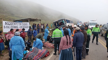 Vista de un accidente de bus en una carretera montañosa y neblinosa de Cusco, Perú, con personal de emergencia, policía y civiles atendiendo a heridos.