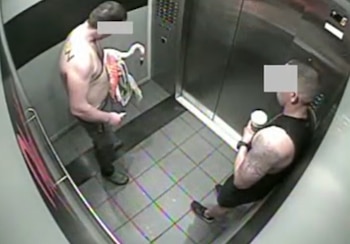 Dos hombres con los rostros cubiertos dentro de un ascensor, uno de ellos sin camiseta sostiene un flamenco y el otro lleva un vaso