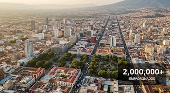 Vista aérea de una ciudad con edificios, una avenida central, áreas verdes y montañas al fondo; se lee '2,000,000+ EMPADRONADOS'.