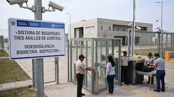 Un cartel de control de seguridad, guardias junto a un torniquete biométrico y un escáner de equipaje frente a un edificio moderno.