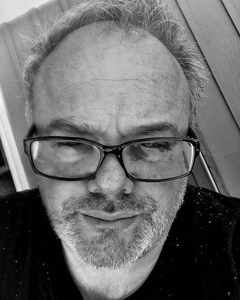 Retrato en blanco y negro de un hombre con gafas y barba, en plano picado. El hombre mira directamente a cámara