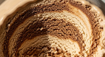 Imagen de cerca de la textura interna de un helado de café y leche de almendras, mostrando patrones arremolinados en tonos marrón claro y oscuro.