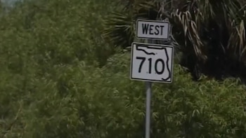 Una señal de tráfico blanca y negra para 'WEST' y la carretera estatal 710 de Florida, con el contorno del estado, rodeada de densa vegetación