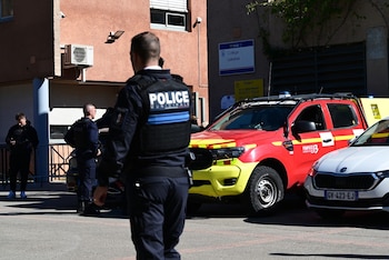 Agentes de policía de espaldas, un vehículo de bomberos rojo y amarillo, varios automóviles y un cartel de la escuela Collège Lakanal
