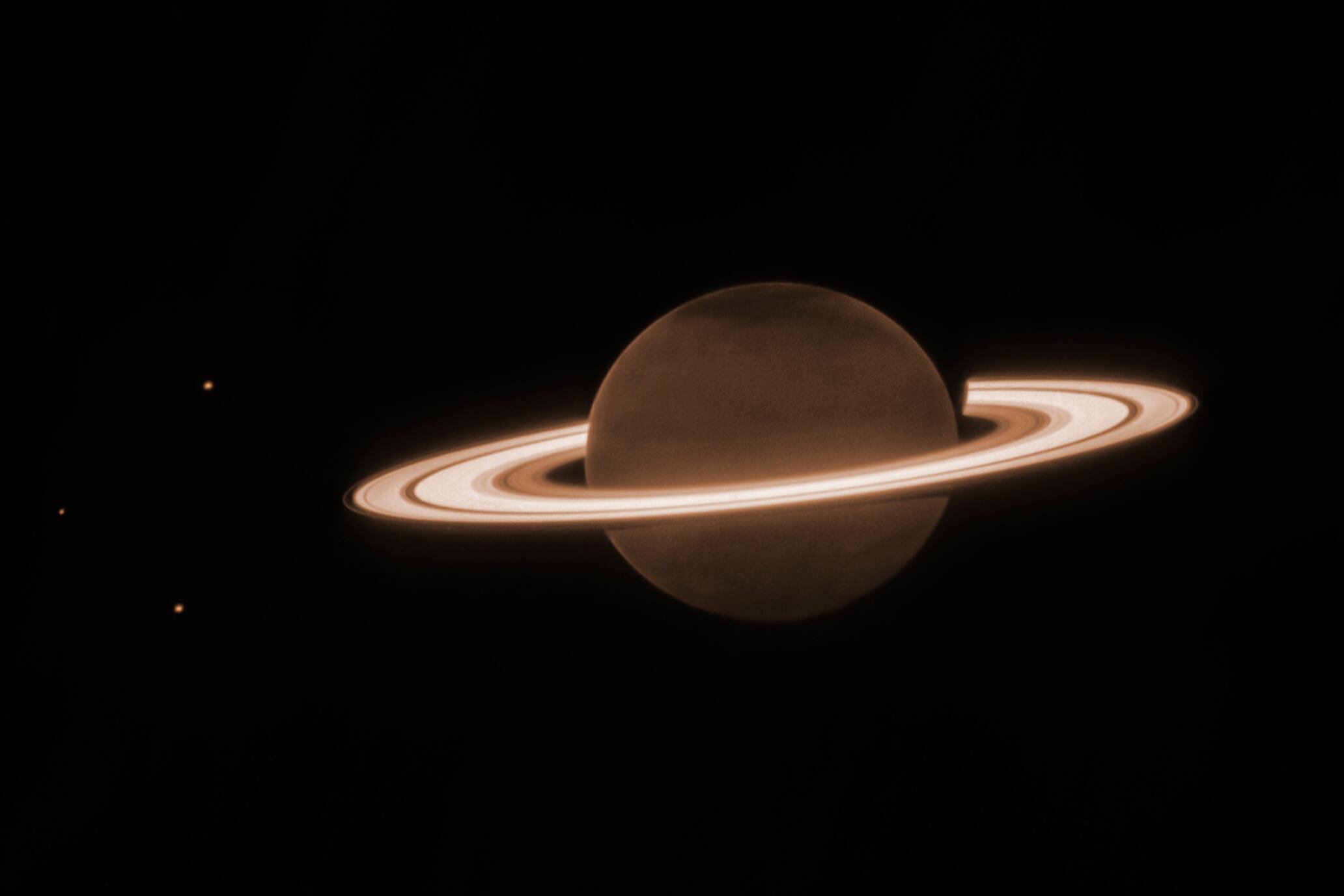 Esta imagen de junio de 2023 suministrada por el Instituto de Ciencia del Telescopio Espacial muestra al planeta Saturno y tres de sus lunas (Encélado, Tetis y Dione) capturados por el Telescopio Espacial James Webb. En infrarrojo, el planeta se ve obscuro porque la luz solar es absorbida por el metano de la atmósfera. (NASA, ESA, CSA, JWST Saturn Team vía AP)