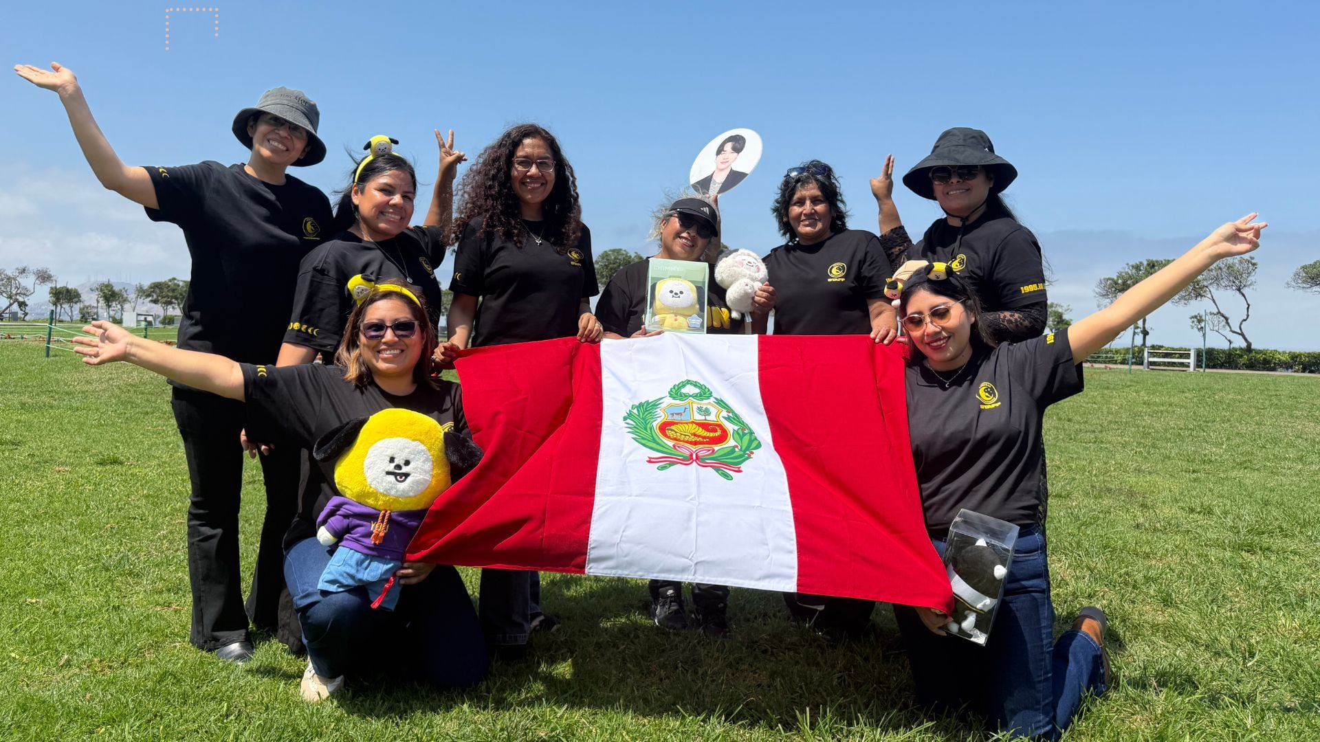 Integrantes del club de fans de Jimin, PJmusas, posan al aire libre con camisetas negras, artículos temáticos del cantante y la bandera de Perú. (Paula Arias)