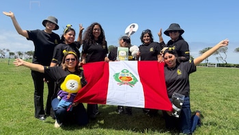 Grupo de mujeres vestidas con camisetas negras sostiene la bandera de Perú sobre un campo de césped verde