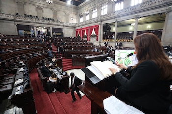 Interior del Congreso de la República con numerosos legisladores sentados en filas de madera. Una operadora de espaldas maneja un panel electrónico de votación