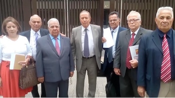 Un grupo de siete abogados, seis hombres y una mujer, de pie frente a un edificio. La mayoría viste ropa formal, y algunos sostienen documentos en sus manos