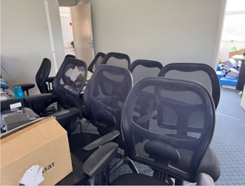 Interior de una oficina con sillas de malla negras. En primer plano, una caja de cartón sobre un escritorio. Al fondo, pilas de documentos y una puerta abierta