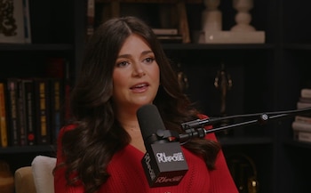Mujer con cabello oscuro y blusa roja hablando a un micrófono con el logo 'On Purpose' en un estudio con estanterías llenas de libros