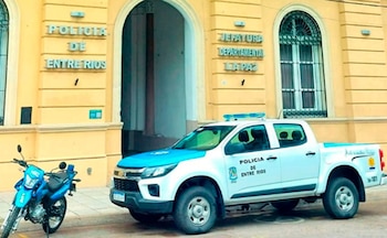 Fachada amarela da Sede do Departamento de Entre Ríos em La Paz com carros de polícia e motocicletas estacionados em frente