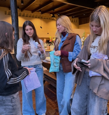 Cuatro mujeres de pie sostienen y revisan bolsas de regalo de papel y plástico dentro de una galería techada