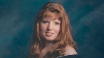 Retrato de una mujer joven con cabello rojizo suelto, flequillo y una blusa oscura, sonriendo ligeramente frente a un fondo azulado
