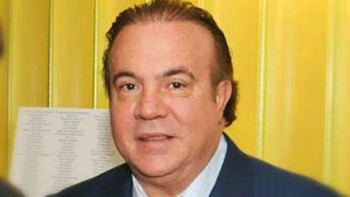 Retrato de un hombre de mediana edad, tez clara y cabello oscuro peinado hacia atrás, vistiendo un traje oscuro y camisa clara, sobre fondo amarillo