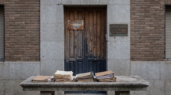 Puerta de madera, cartel "Propiedad Privada", placa "Registro Público de la Propiedad", legajos de documentos en banco de piedra.