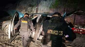 Varias personas con rostros borrosos permanecen sentadas a una mesa mientras agentes de policía las supervisan de noche
