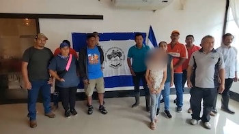 Un grupo de personas permanece de pie en una habitación delante de dos banderas colgadas en la pared