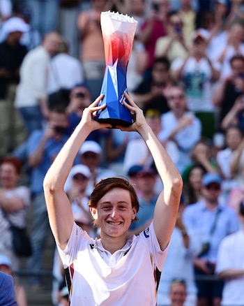 Ignacio Buse sonríe, levantando un trofeo bicolor (rojo y azul) sobre su cabeza, con una multitud de espectadores de fondo borrosa