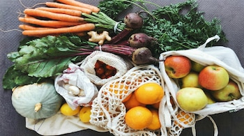 Vista aérea de varias frutas y verduras frescas como zanahorias, remolachas, jengibre, calabaza, champiñones, limones, tomates cherry, naranjas y manzanas sobre una superficie gris.