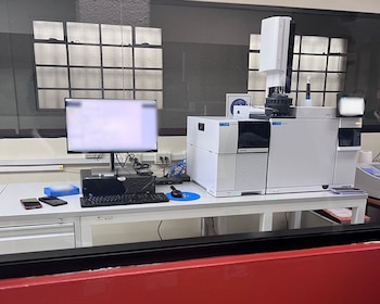 Equipo cromatógrafo de líquidos y espectrómetro de masas (LC-MS) en un laboratorio forense, con un monitor y teclado sobre un escritorio blanco