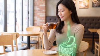 Una mujer con cabello oscuro y blusa clara sostiene una taza de té. Su sistema digestivo está ilustrado en color verde sobre su torso en un café.