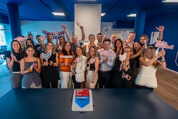 Un grupo de treinta personas en una oficina sonríe y sostiene carteles de celebración. Un pastel en primer plano dice 'Great Place To Work Certified LOGRAR'